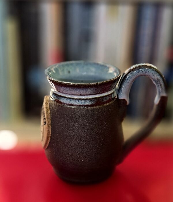 close up of mug, side profile, with blue glaze breaking brown over texture on rim and top of handle.