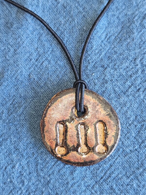 circular pendant with shiny copper glaze and three exclamation marks, imprinted and unglazed