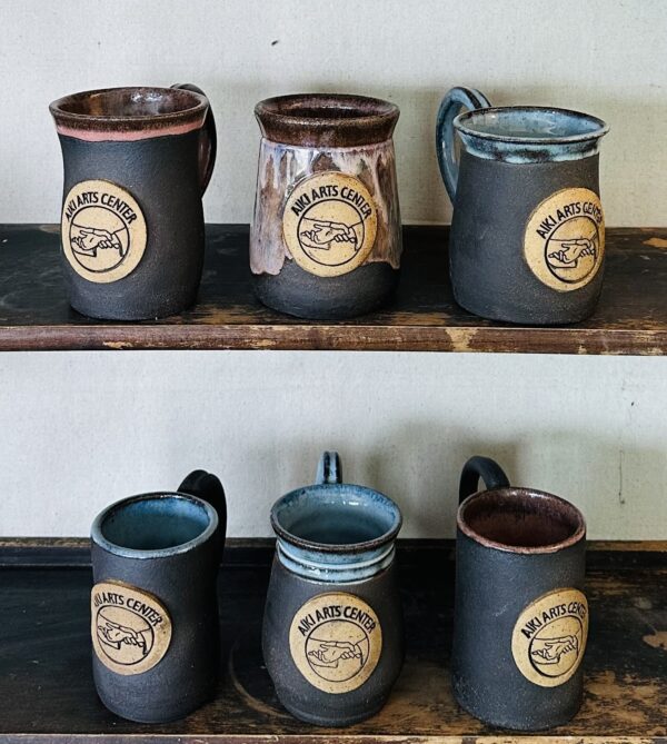 mugs with charcoal claybody, glossy pink or blue glaze inside and around rim, and circular Aiki Arts Center logo in relief in center