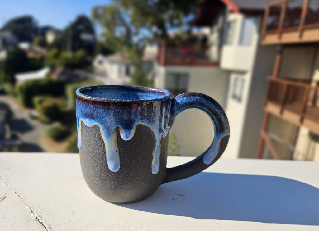 Small mug, unglazed dark brown exterior with vibrant blue interior dripping around rim