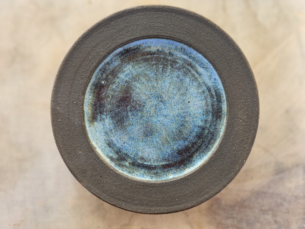 Round plate with dark brown, unglazed rim and vibrant blue, fluxy glaze in the middle