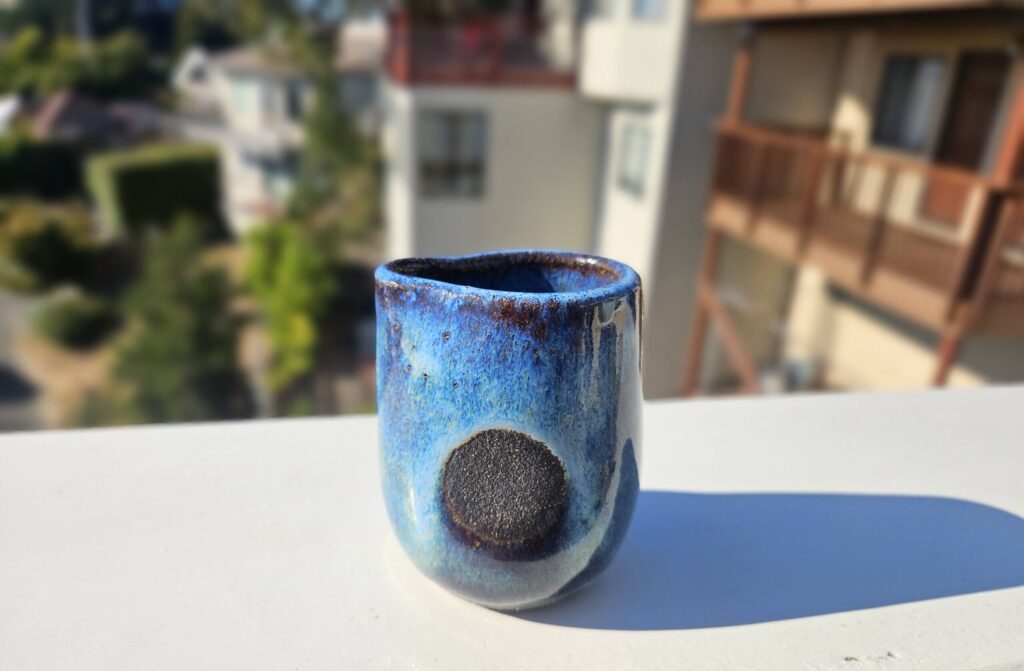 Small pitcher glazed blue breaking over very dark brown/black over rim, with very dark unglazed circle on the side indented for thumb and finger